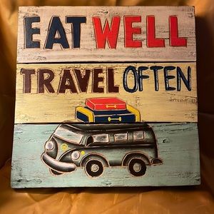 Wooden sign- says “eat well & travel often” and it has a van w/luggage on top